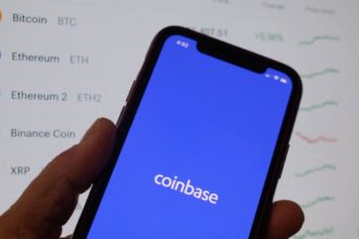 Coinbase's logo on a phone in front of crypto prices